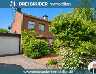 Ein zweigeschossiges, rotes Wohnhaus mit grünen Büschen und Blumen im Vordergrund. Links befindet sich eine Garage mit einem Rolltor. Der Garten ist gepflegt und bietet eine einladende Atmosphäre.